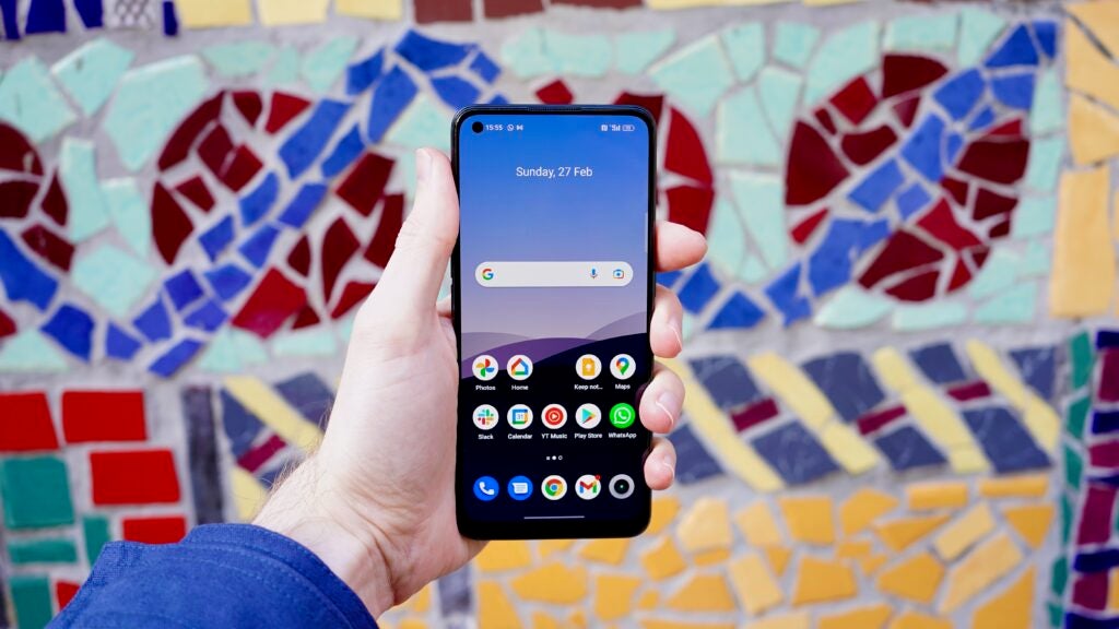 Realme 9 Pro Plus home screen helf up before a tiled wall